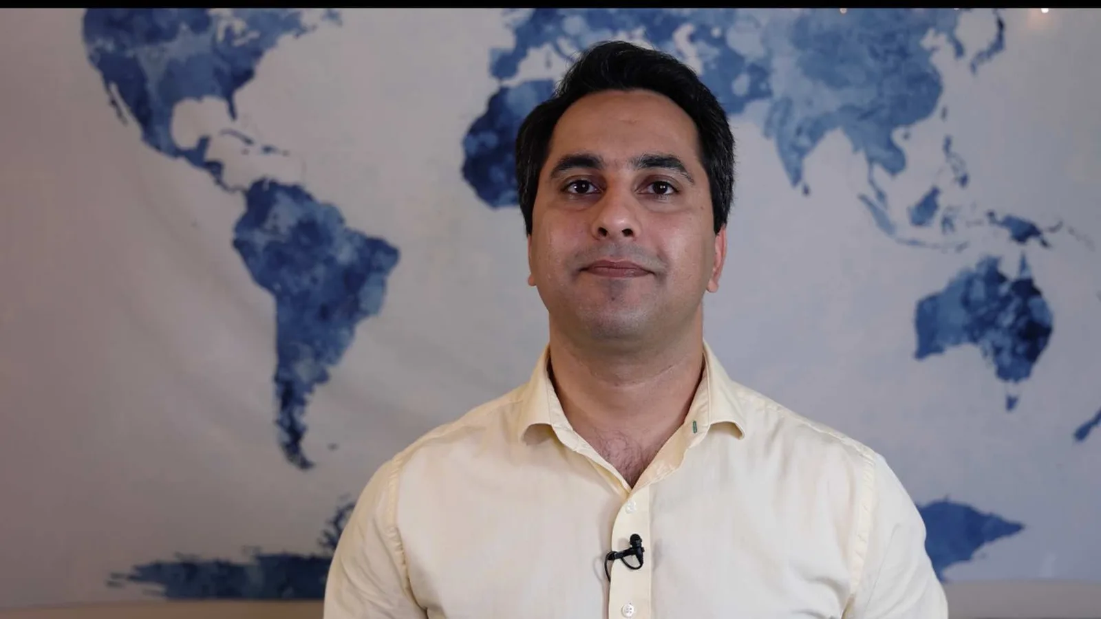 A man speaking in front of a world map.