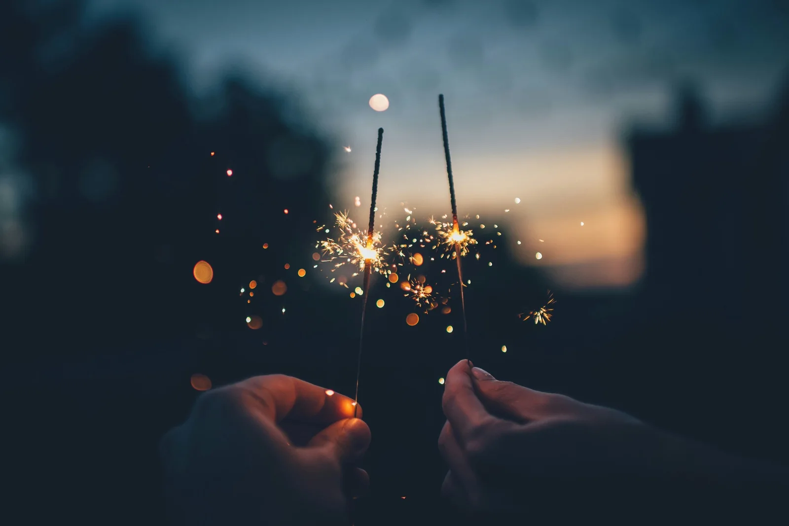 Two people holding lit sparklers at dusk.