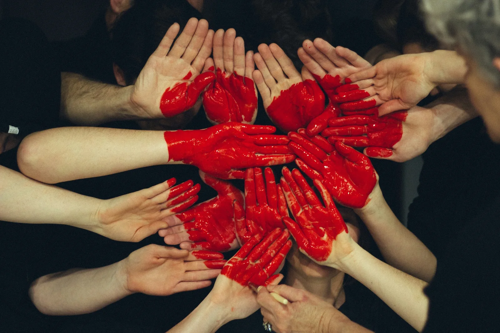 Several hands covered with red paint forming a circle.