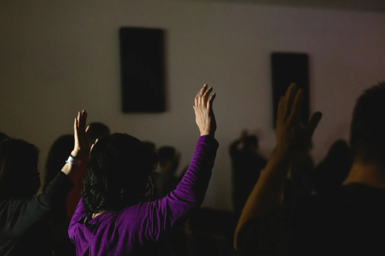 People raising their hands in a dimly lit room.