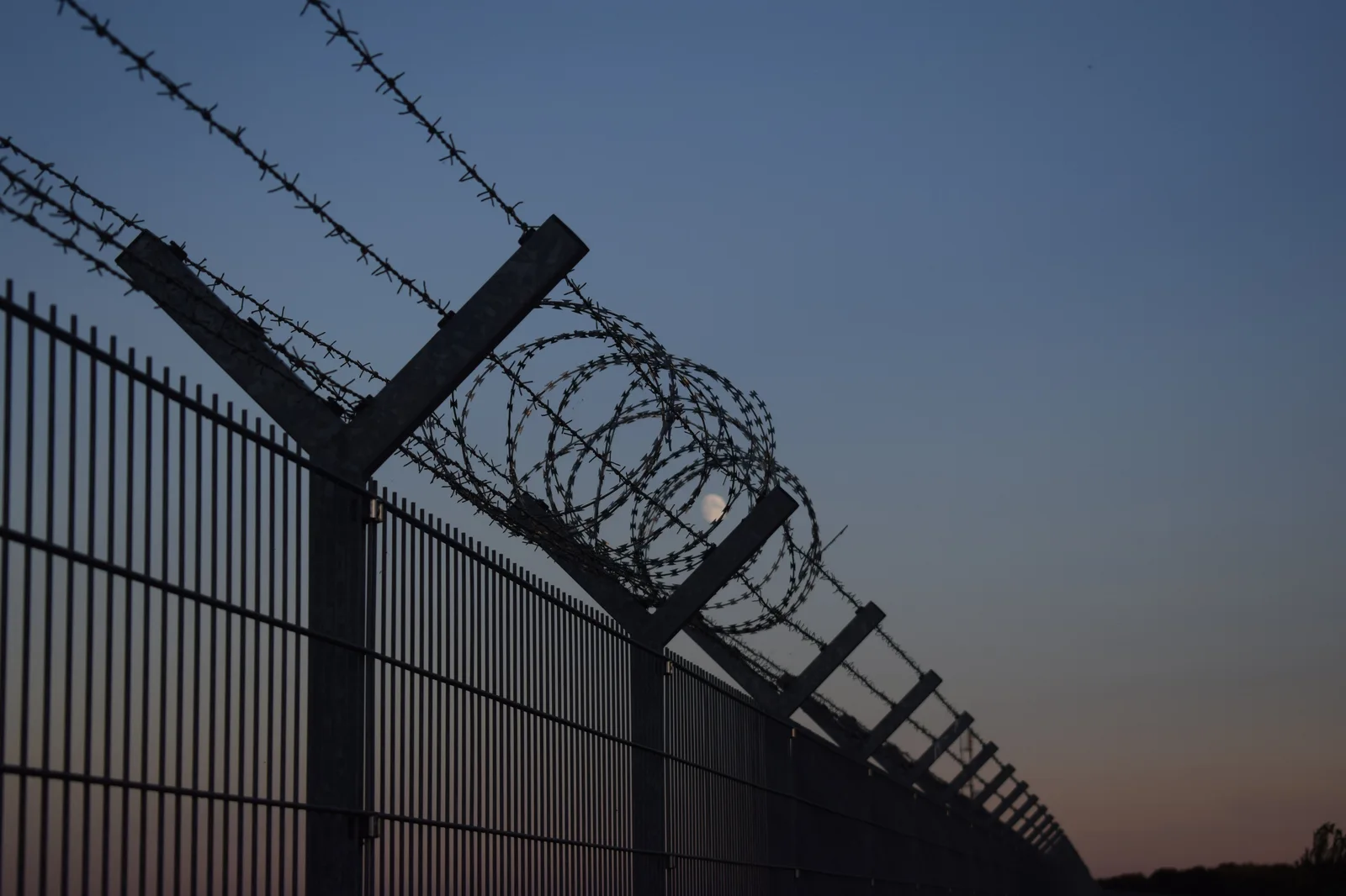 Tall metal fence topped with coils of razor wire.