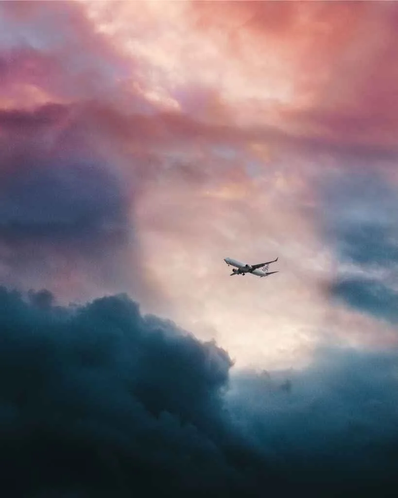 Airplane flying beneath pink and blue clouds.