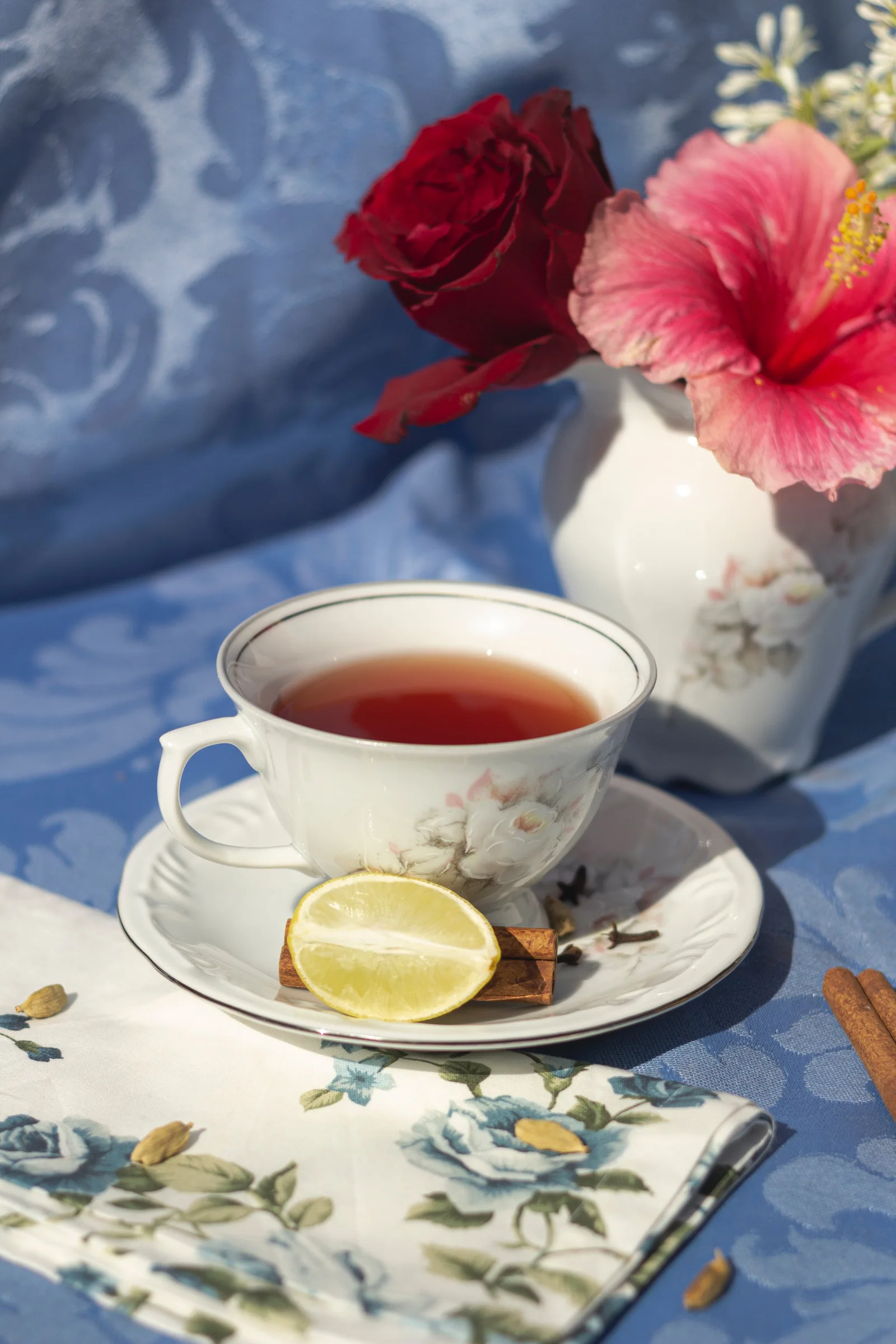 Cup of tea with lemon beside flowers.